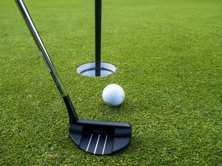 Putter and golf ball near the cup on a putting green