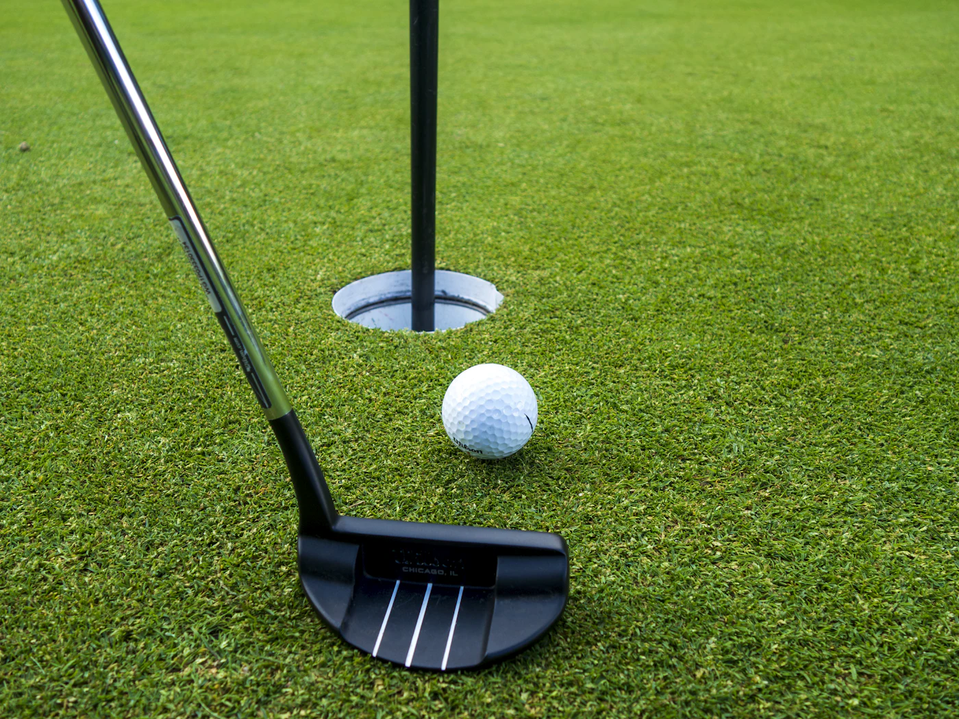 Putter and golf ball near the cup on a putting green
